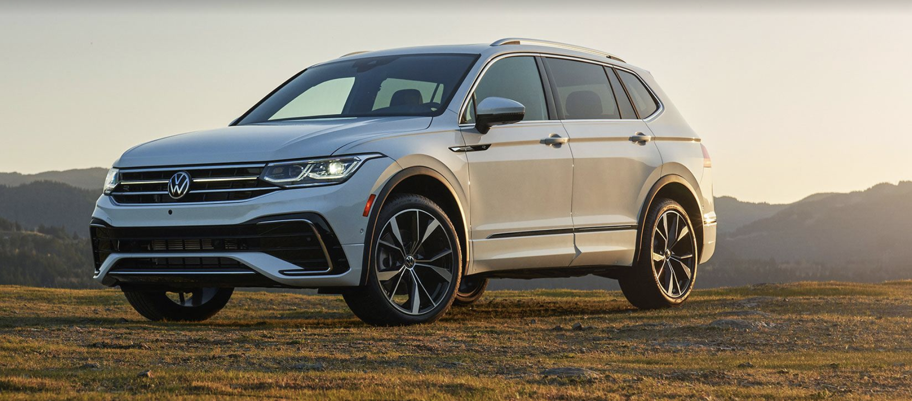 2022 Tiguan parked in a field with the sun shining down and a mountain range in the background.
