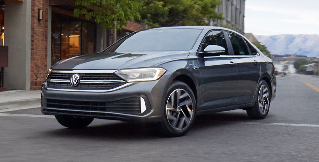 Jetta parked on a city street with the sun setting in the background.
