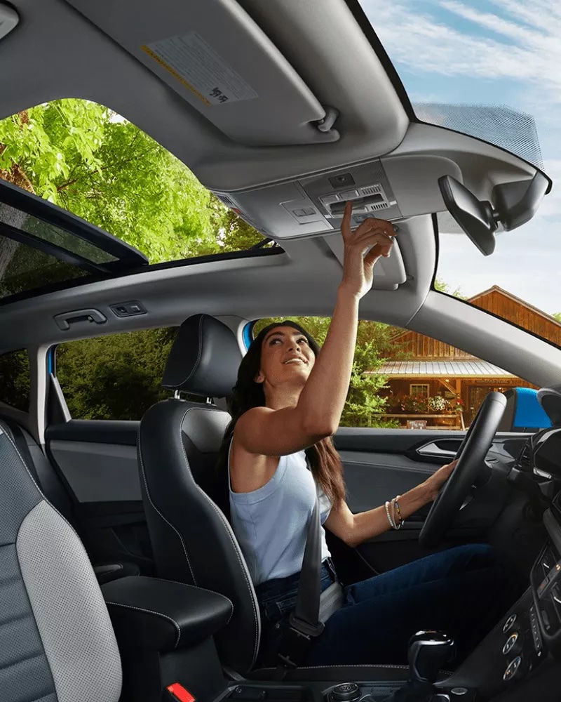 A woman in her Volkswagen vehicle adjusting the sunroof